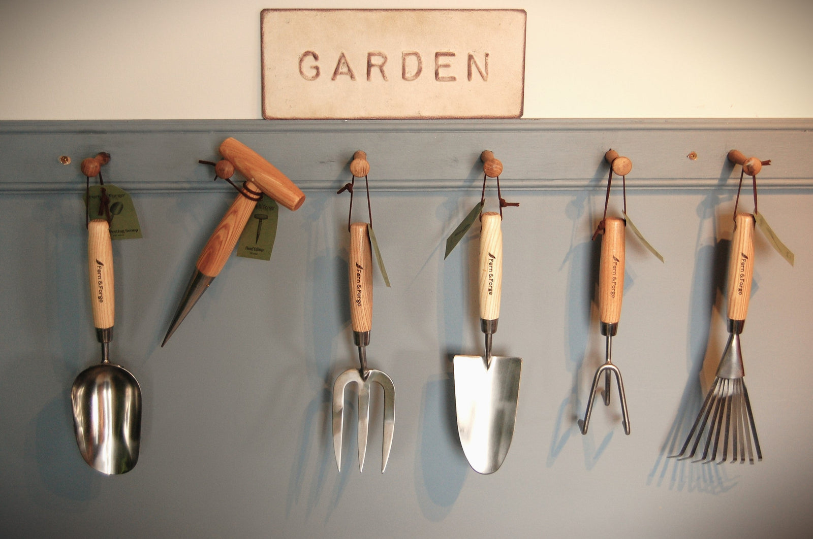 Set of gardening tools hanging on a wall with a sign above reading 'Garden'.