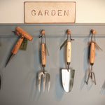 Set of gardening tools hanging on a wall with a sign above reading 'Garden'.